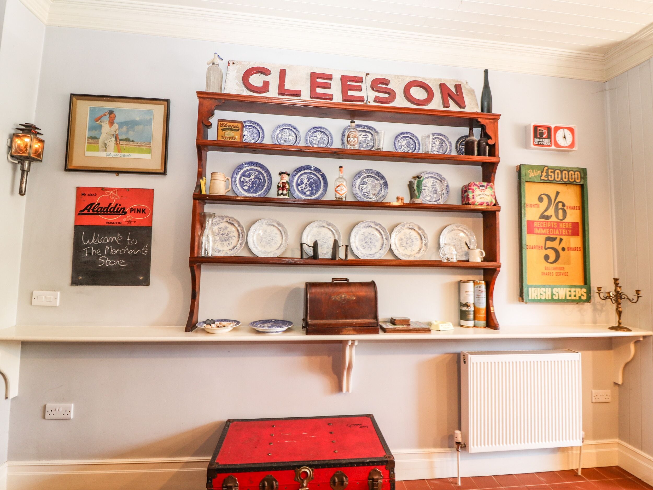 A shelf with various dishes and a red trunk.