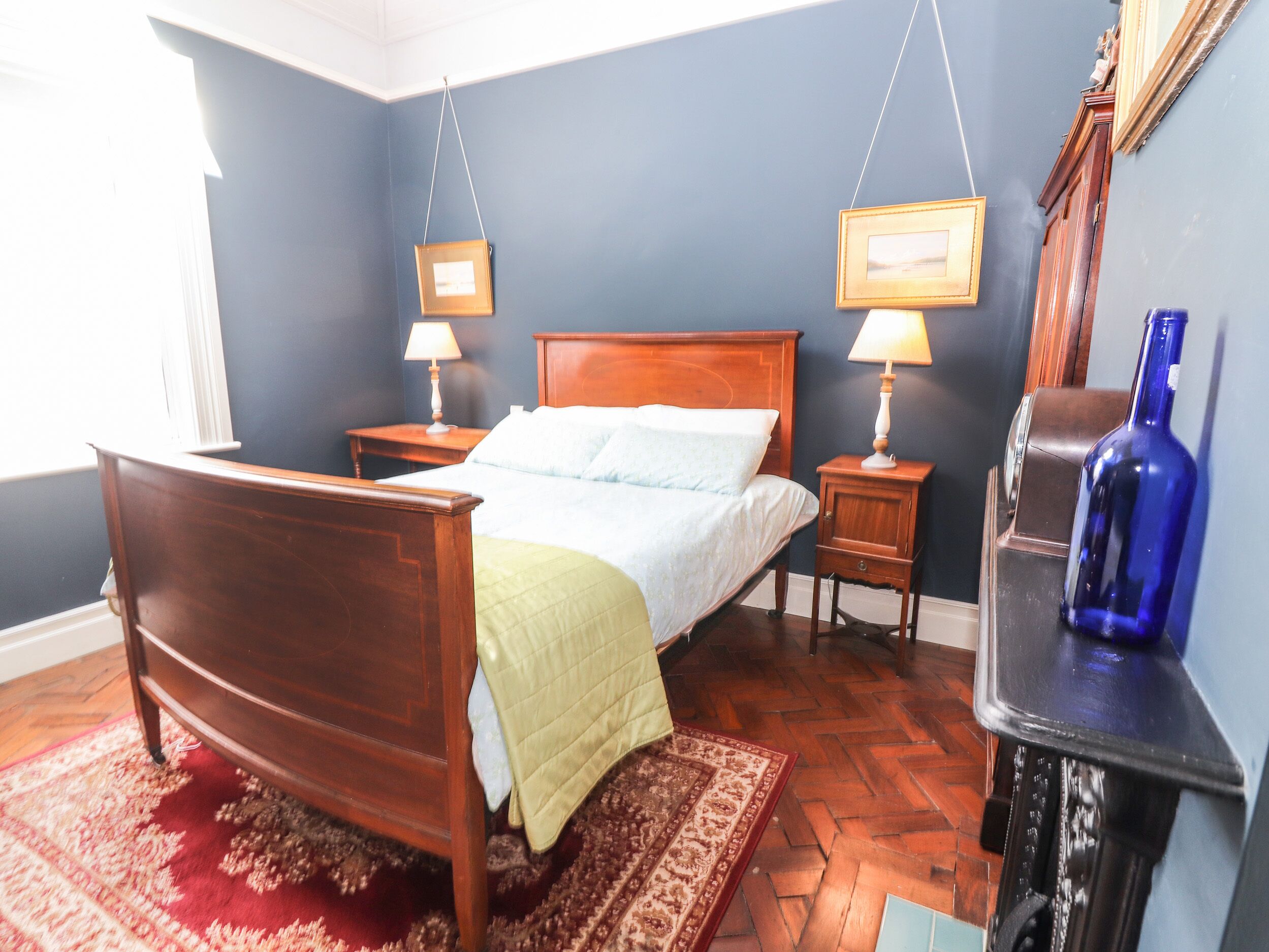Ein Schlafzimmer mit einem hölzernen Bett, zwei Nachttischen mit Lampen, einer blauen Wand und einem roten Teppich.