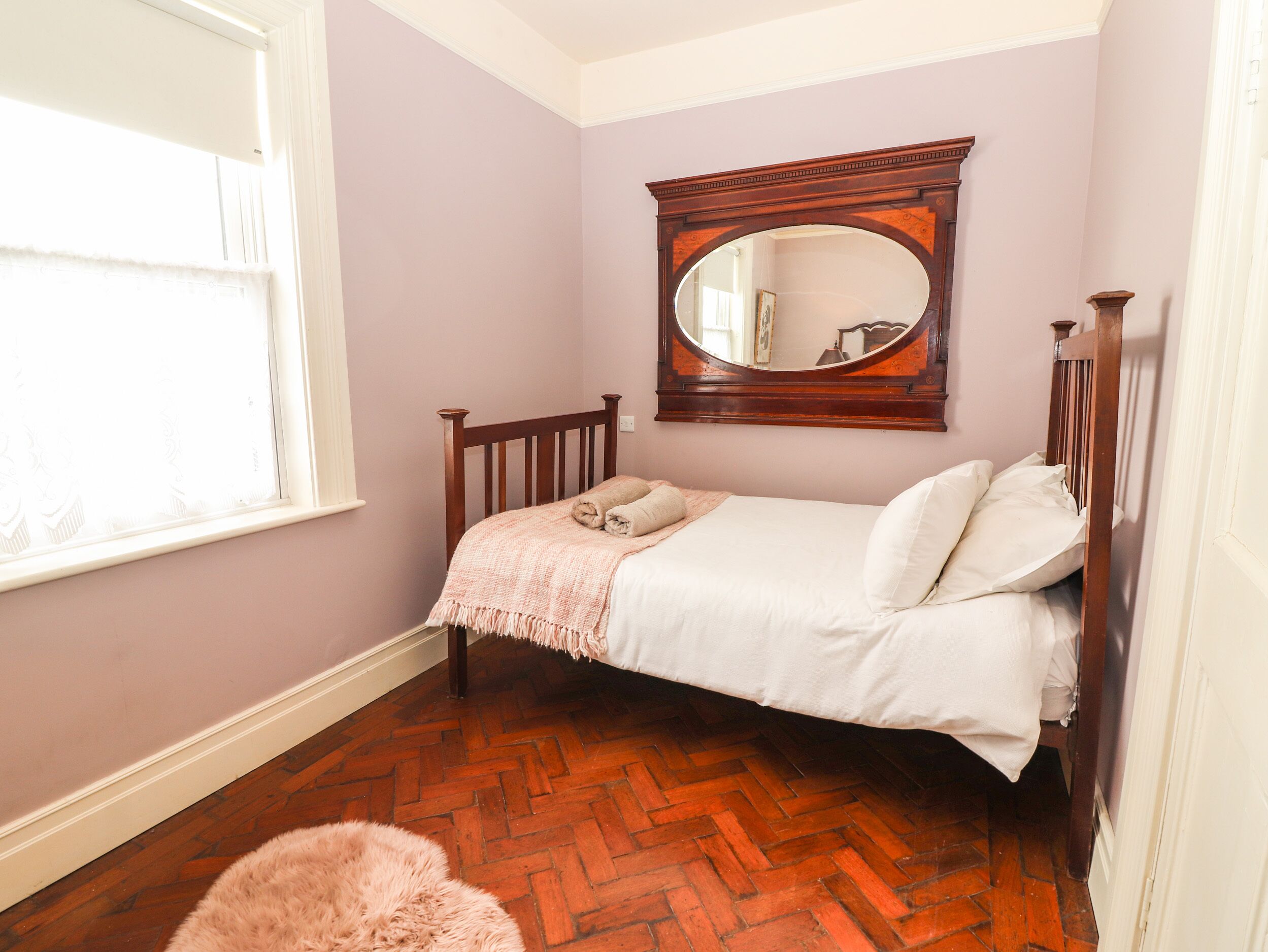 Un dormitorio con una cama de madera, un espejo grande y un suelo con estampado de espiga.