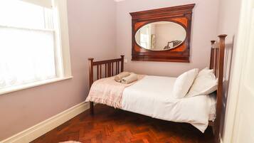 Un dormitorio con una cama de madera, un espejo grande y un suelo con estampado de espiga.