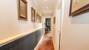 A hallway with a herringbone patterned wooden floor, white walls, and framed artwork on the walls. - The Merchant's Store (Kilrush)