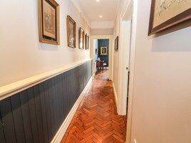 A hallway with a herringbone patterned wooden floor, white walls, and framed artwork on the walls.