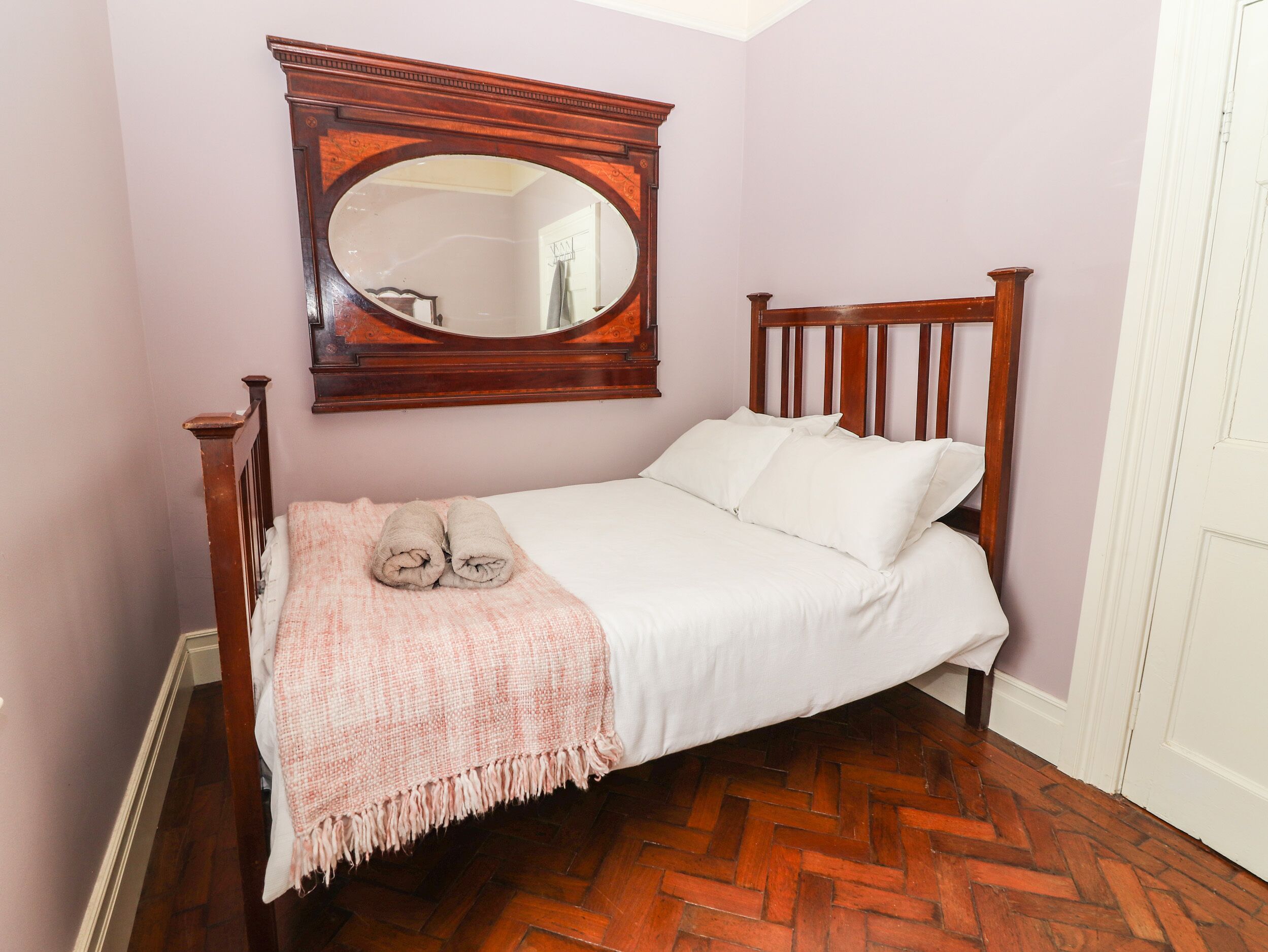 Una cama bien arreglada con cabecera de madera, una manta rosa y un espejo grande encima.