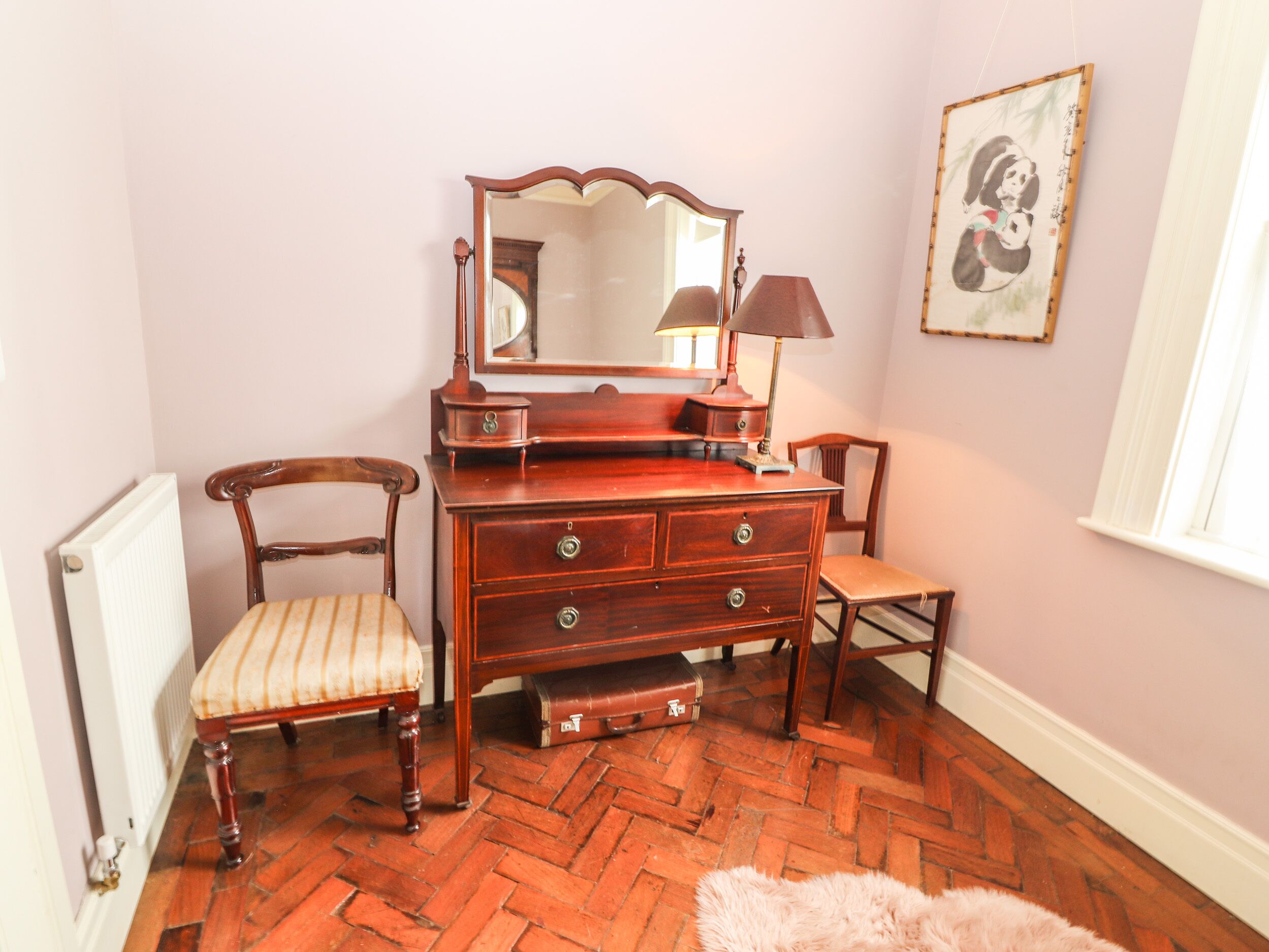 Une pièce comprenant une commode en bois, une chaise, une petite table et un radiateur.