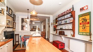 A cozy kitchen with a wooden table, a red trunk, and a shelf with dishes. - The Merchant's Store (Kilrush)