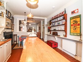 A cozy kitchen with a wooden table, a red trunk, and a shelf with dishes.