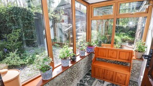 Une véranda avec un banc en bois, des murs en pierre et des plantes en pot sur le rebord de la fenêtre.
