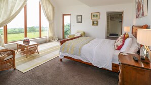 A bedroom with a large bed, a wooden nightstand, a chair, a window with curtains, and a door leading to a balcony. - Millers Lane House (Muff)