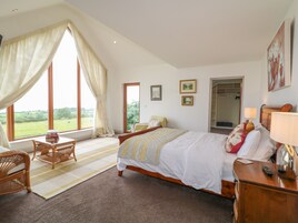 A bedroom with a large bed, a wooden nightstand, a chair, a window with curtains, and a door leading to a balcony.