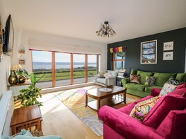 A living room with a green sofa, a red armchair, and a wooden coffee table. There is a large window with a view of a lake and mountains.