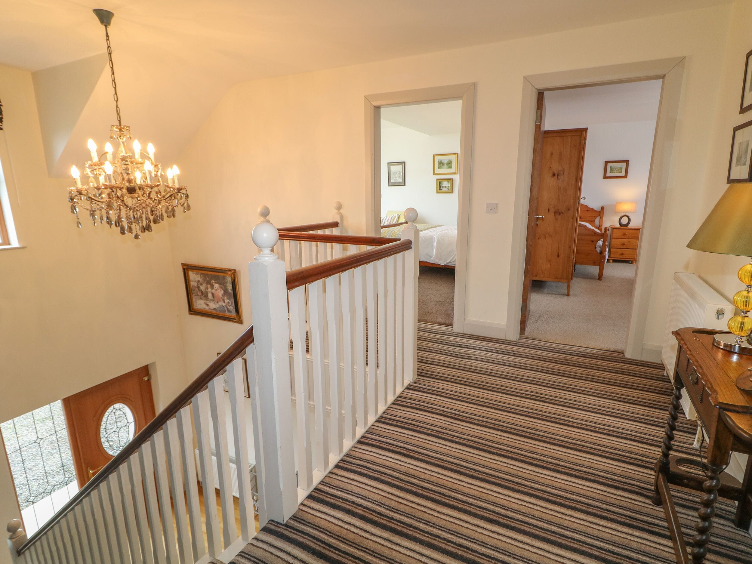 A staircase with a striped carpet, a chandelier, and a wooden door leading to a bedroom.
