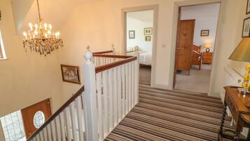 A staircase with a striped carpet, a chandelier, and a wooden door leading to a bedroom.