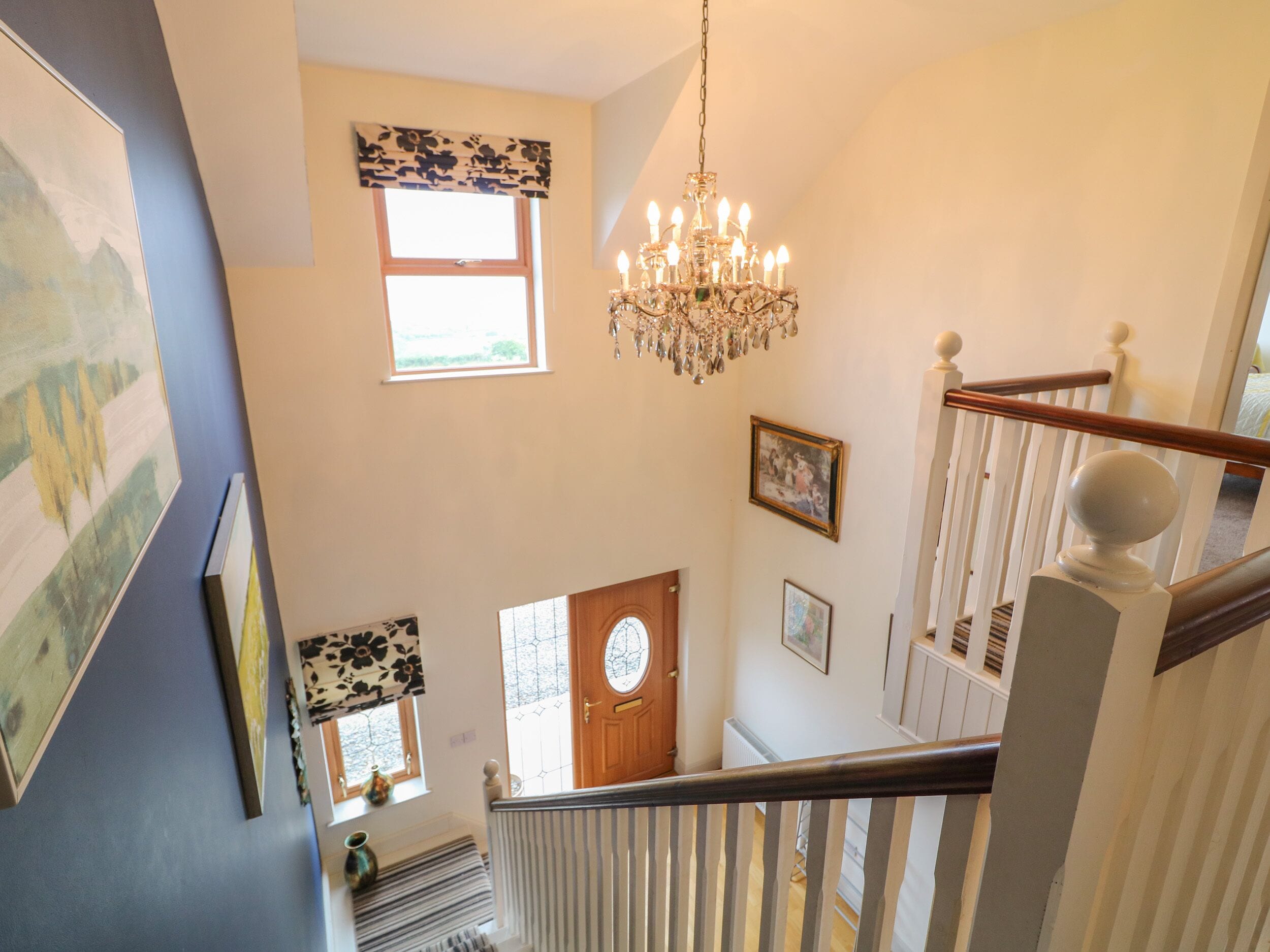 A staircase with a chandelier, a wooden door, and a window with a floral valance.