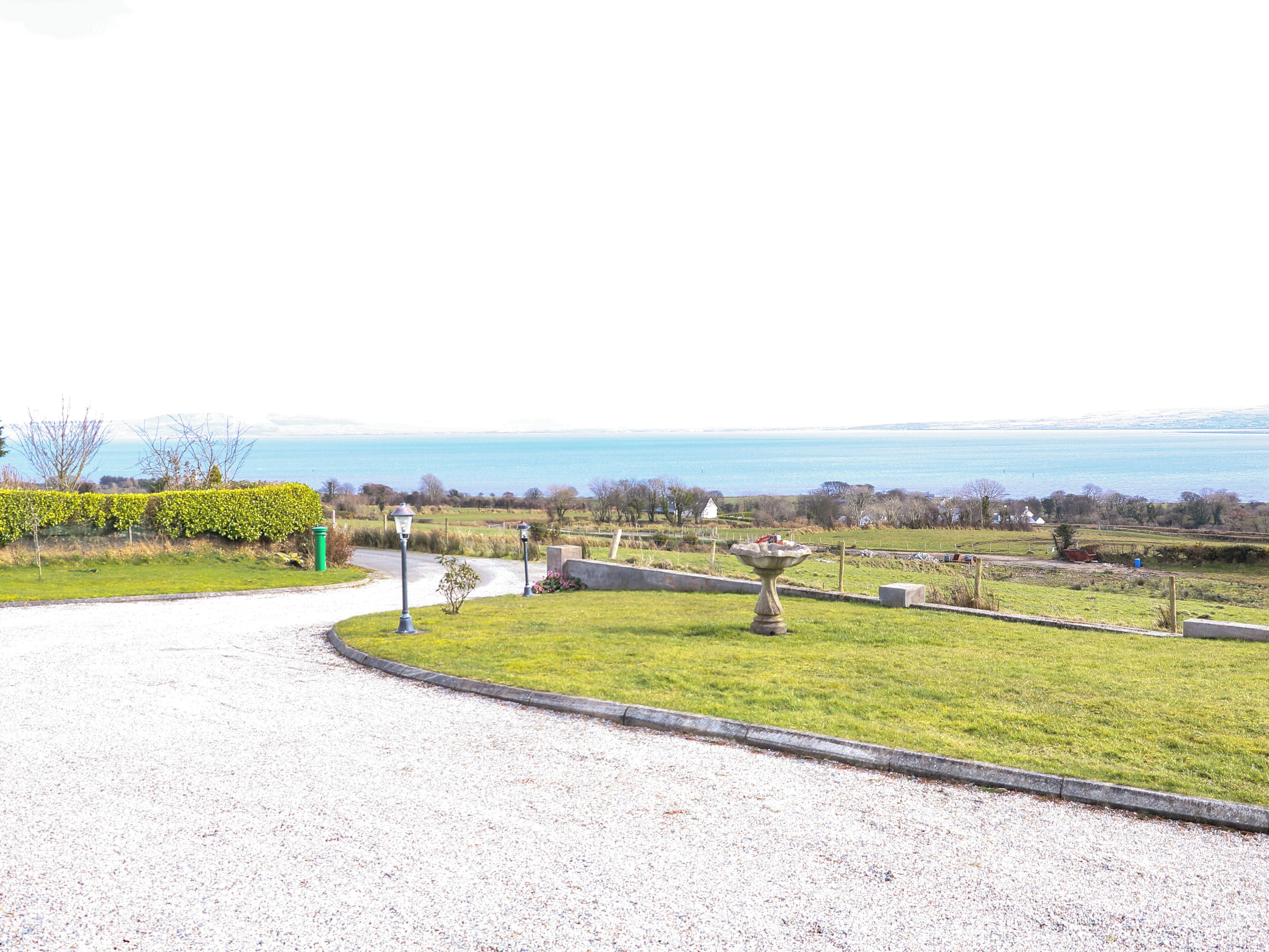 A gravel driveway leading to a grassy area with a birdbath and a lamp post.