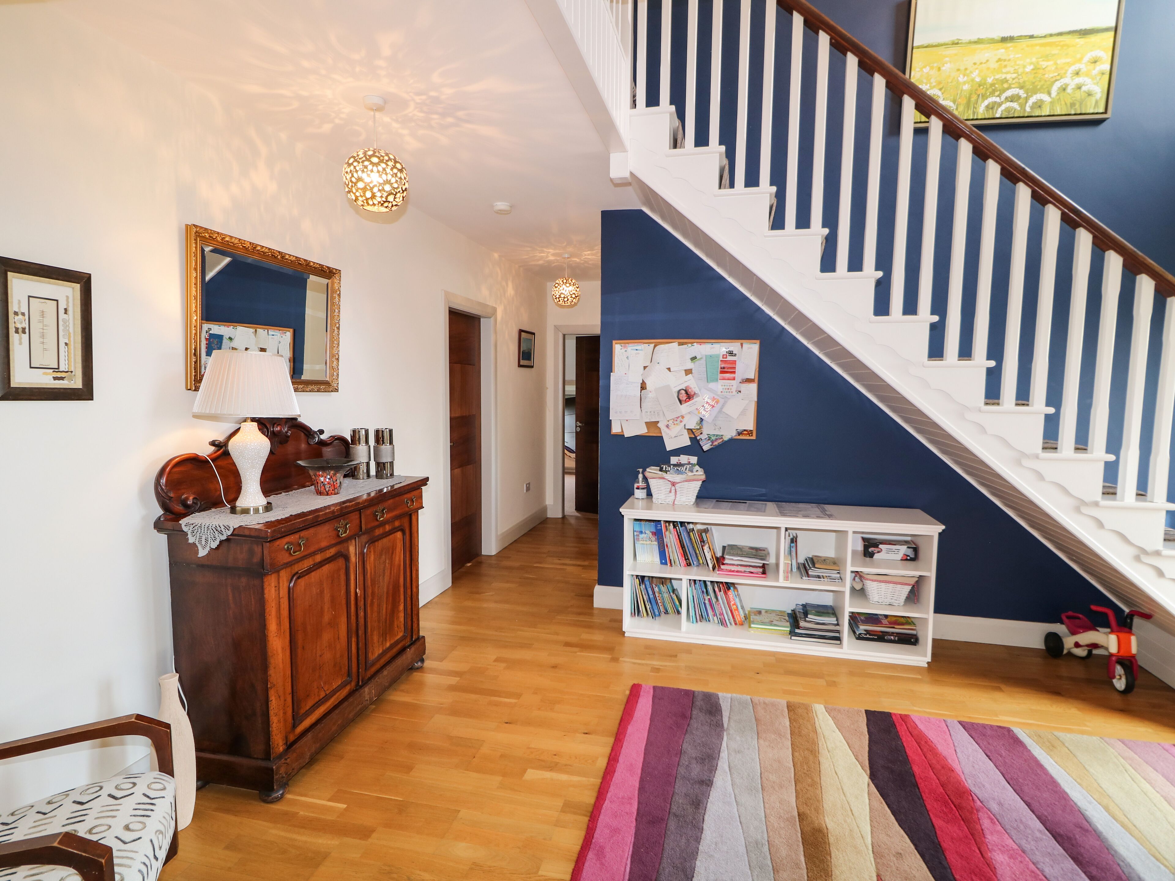 A spacious living area with a wooden floor, a staircase, a bookshelf, and a decorative mirror.