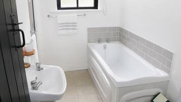 A bathroom with a white sink, a bathtub, and a window.