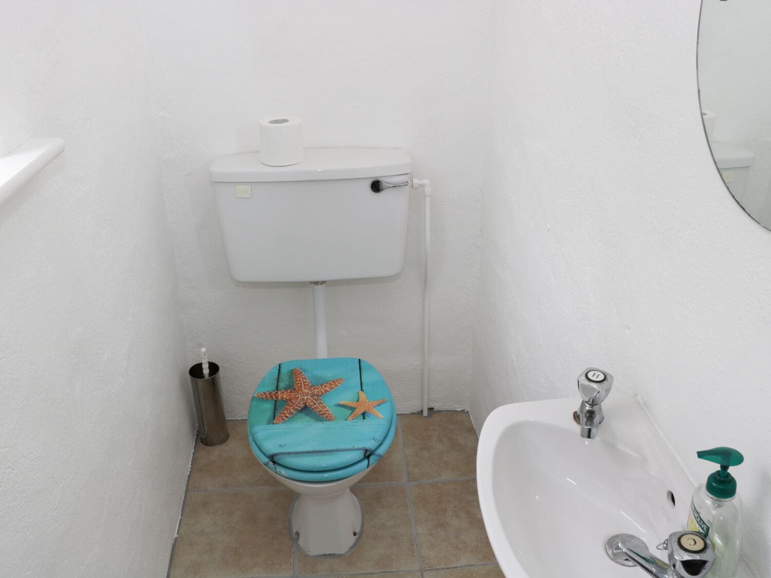 Un baño con inodoro, lavabo y una decoración de estrella de mar en el asiento del inodoro.