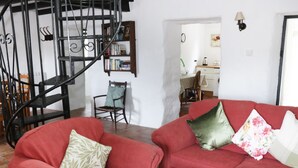 Een woonkamer met twee rode banken, een houten salontafel, een zwart spiraaltrap, een boekenkast en een eethoek op de achtergrond.