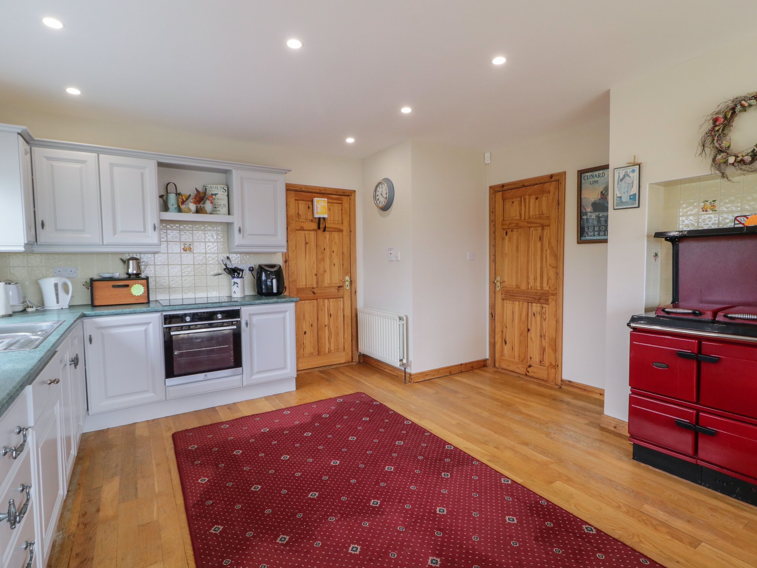 A kitchen with white cabinets, a red stove, and a wooden floor.