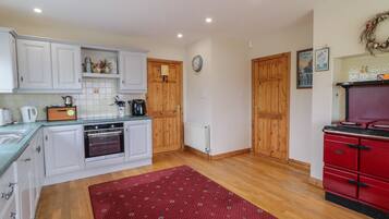A kitchen with white cabinets, a red stove, and a wooden floor.