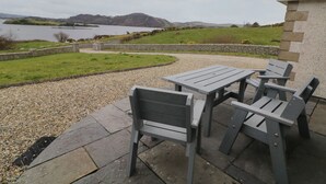 An outdoor patio with a table and chairs, overlooking a lake and hills. - Ranny Roe (Maghernalaght)
