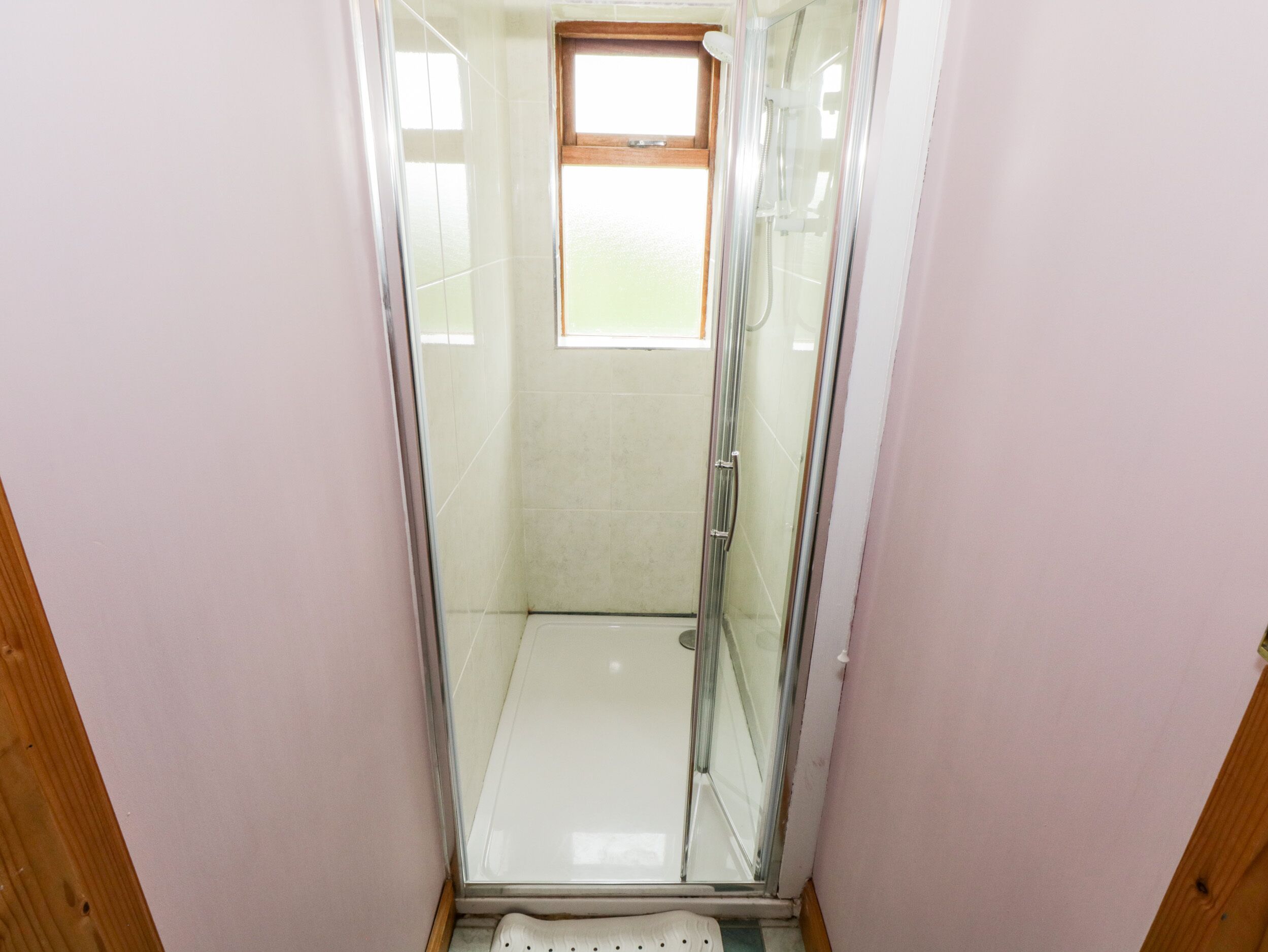 A glass-enclosed shower stall with a window above, wooden walls, and a tiled floor.