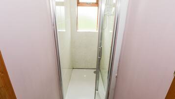 A glass-enclosed shower stall with a window above, wooden walls, and a tiled floor.
