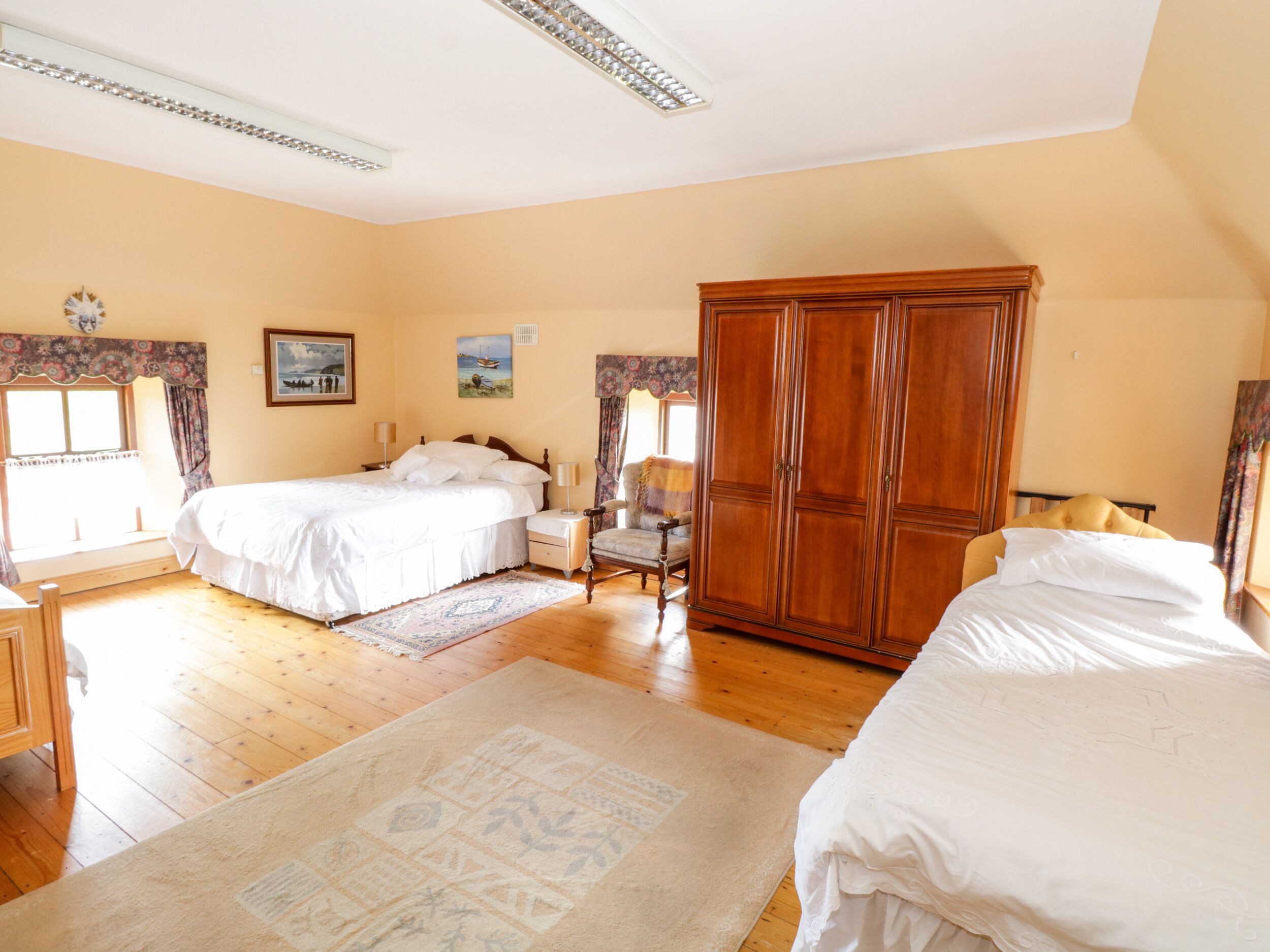 Un dormitorio con dos camas, un armario de madera, una silla y una ventana con cortinas.