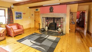 A cozy living room with a fireplace, wooden beams, a sofa, and a rug. - An Maide Bán (Cootehill)