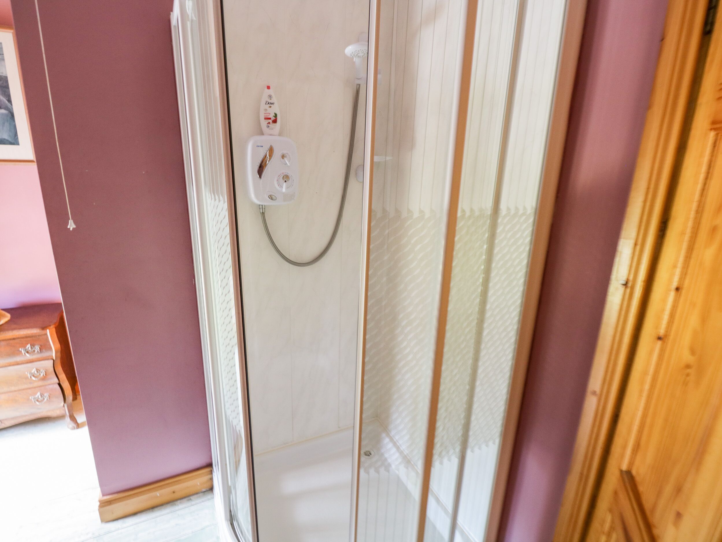 Ducha con mampara de vidrio, cabezal de ducha manual y panel de control.