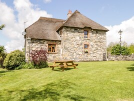 A stone building with a thatched roof, a picnic table, and a stone wall with a gate.