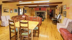 A spacious room with a wooden dining table, chairs, a sofa, and a fireplace. - An Maide Bán (Cootehill)