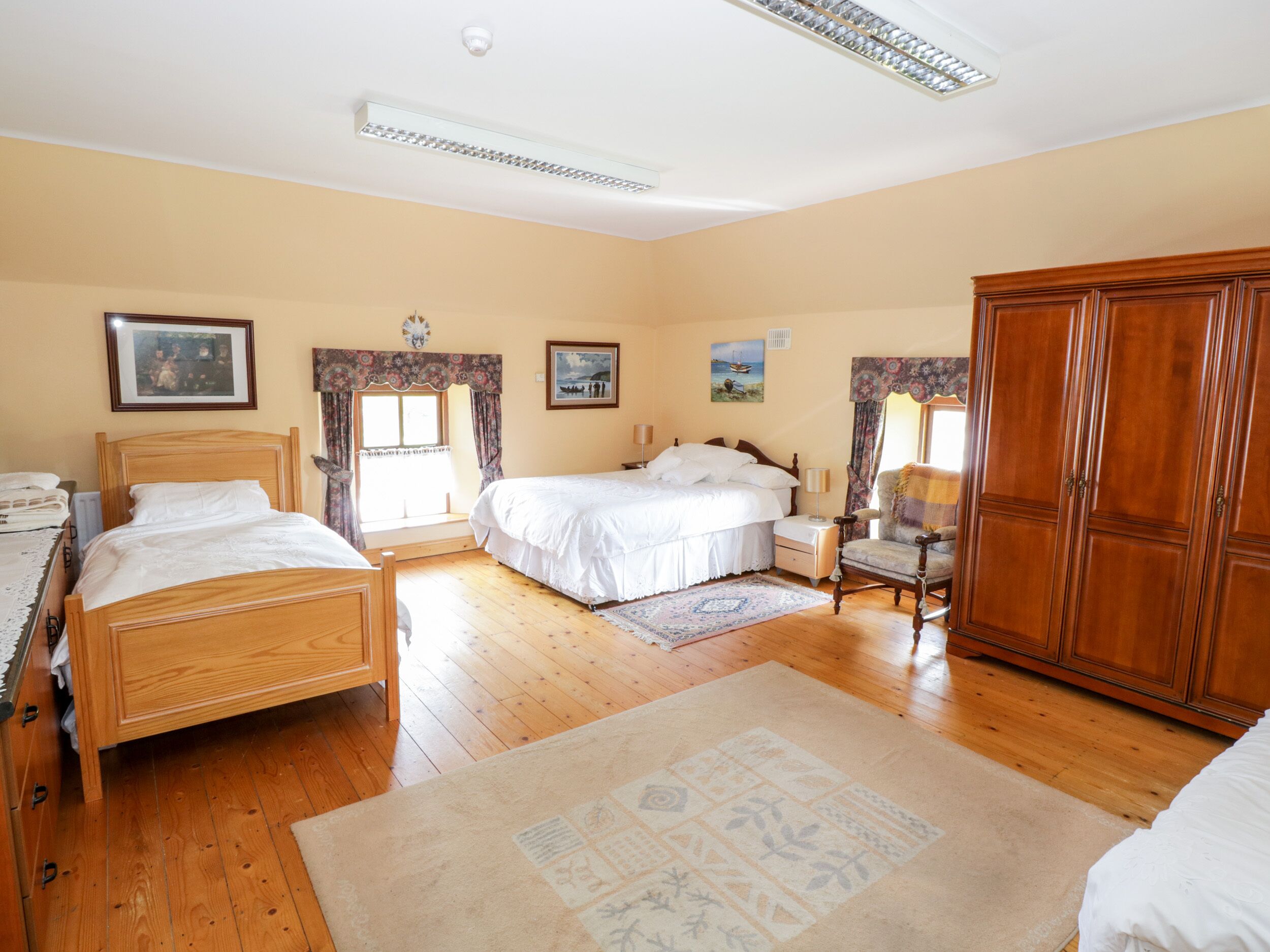 Een slaapkamer met twee eenpersoonsbedden, een houten garderobe en een groot raam met gordijnen.