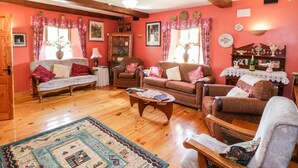 A cozy living room with wooden floors, a variety of seating options including a sofa and armchairs, and a coffee table. - An Maide Bán (Cootehill)