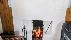 A fireplace with a fire, a wooden mantel, and a clock above it. - The Cottage (Newport)