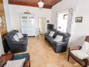 Una sala de estar con dos sofás de cuero negro, un sillón estampado, un aparador azul claro y un televisor sobre una mesita.