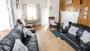 A living room with two black leather sofas, a dining table with chairs, a fireplace, and a wooden ceiling. - The Cottage (Newport)