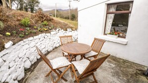 A stone wall, a white building, and a round wooden table with chairs. - The Cottage (Newport)