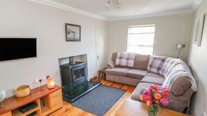 A cozy living room with a sofa, a fireplace, a television, and a wooden coffee table. - Teach Teolai (Carraroe)