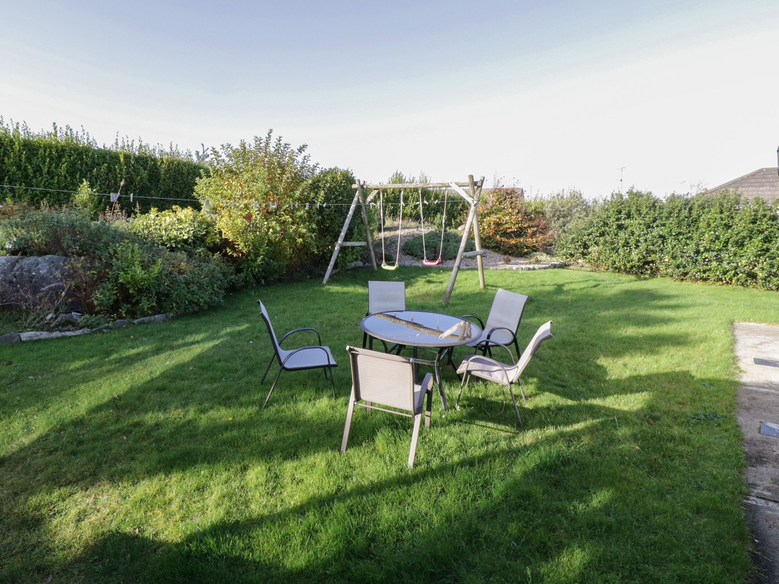 A backyard with a swing set, a round table with four chairs, and a well-maintained lawn.