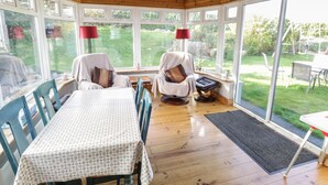 A covered patio area with a wooden ceiling, large windows, a table with chairs, and a bench. - Teach Teolai (Carraroe)