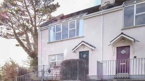 A two-story residential building with a flat roof, a front porch, and a small garden area. - Number 12 (Mulranny)