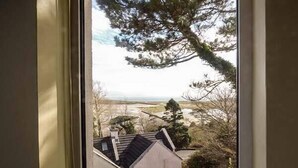A view through a window of a house with a sloped roof, a small garden, and a distant landscape. - Number 12 (Mulranny)