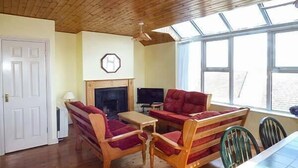 A cozy living room with a fireplace, wooden furniture, and large windows. - Number 12 (Mulranny)