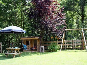 A wooden playhouse, a swing set, and a picnic table with an umbrella in a lush garden. - El Casot, a tranquil retreat with pool in its own valley 30 miles from the sea (Montferrer, Occitanie)