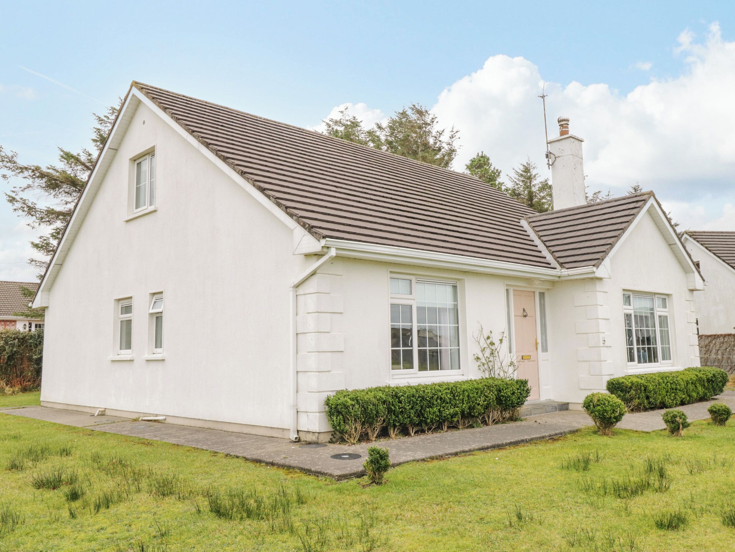 A single-story house with a sloped roof, a front door, and a small front yard with a hedge.