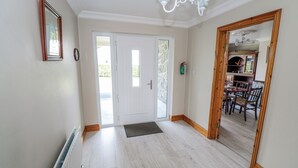A hallway with a white door, a wooden-framed mirror, a radiator, and a dining area visible through the door. - Castle View (Carrowmoreknock)