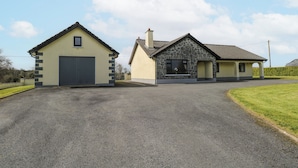 A two-story house with a garage, a stone facade, and a paved driveway. - Castle View (Carrowmoreknock)