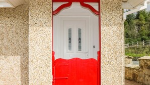 Une porte rouge avec un cadre blanc, intégrée dans un bâtiment aux murs en pierre constellés de taches.