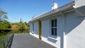 En hvid bygning med en mørk træterrasse, en gul dør og en skorsten.